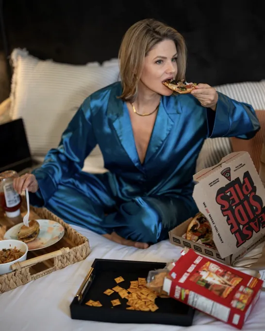 Brittany Watkins in silk pajamas enjoying pizza in bed